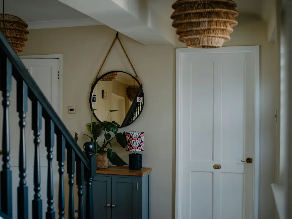 An English hallway with painted stair balusters, a round mirror and a blue-painted cabinet