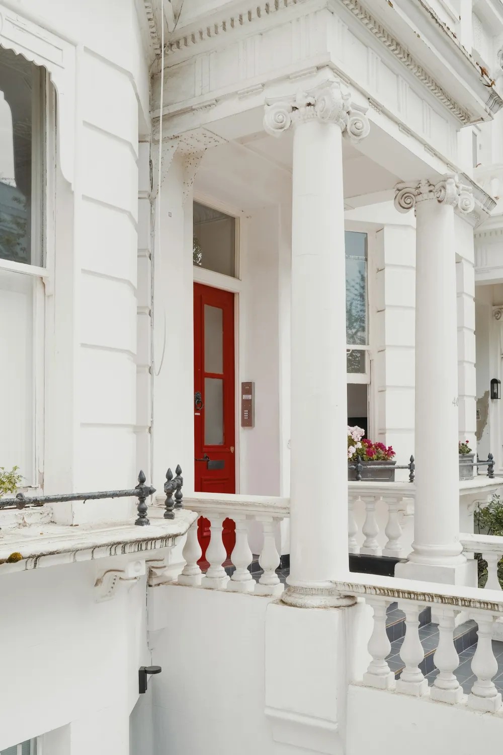 A white stucco terrace in London with a freshly painted red front door and stone balustrade